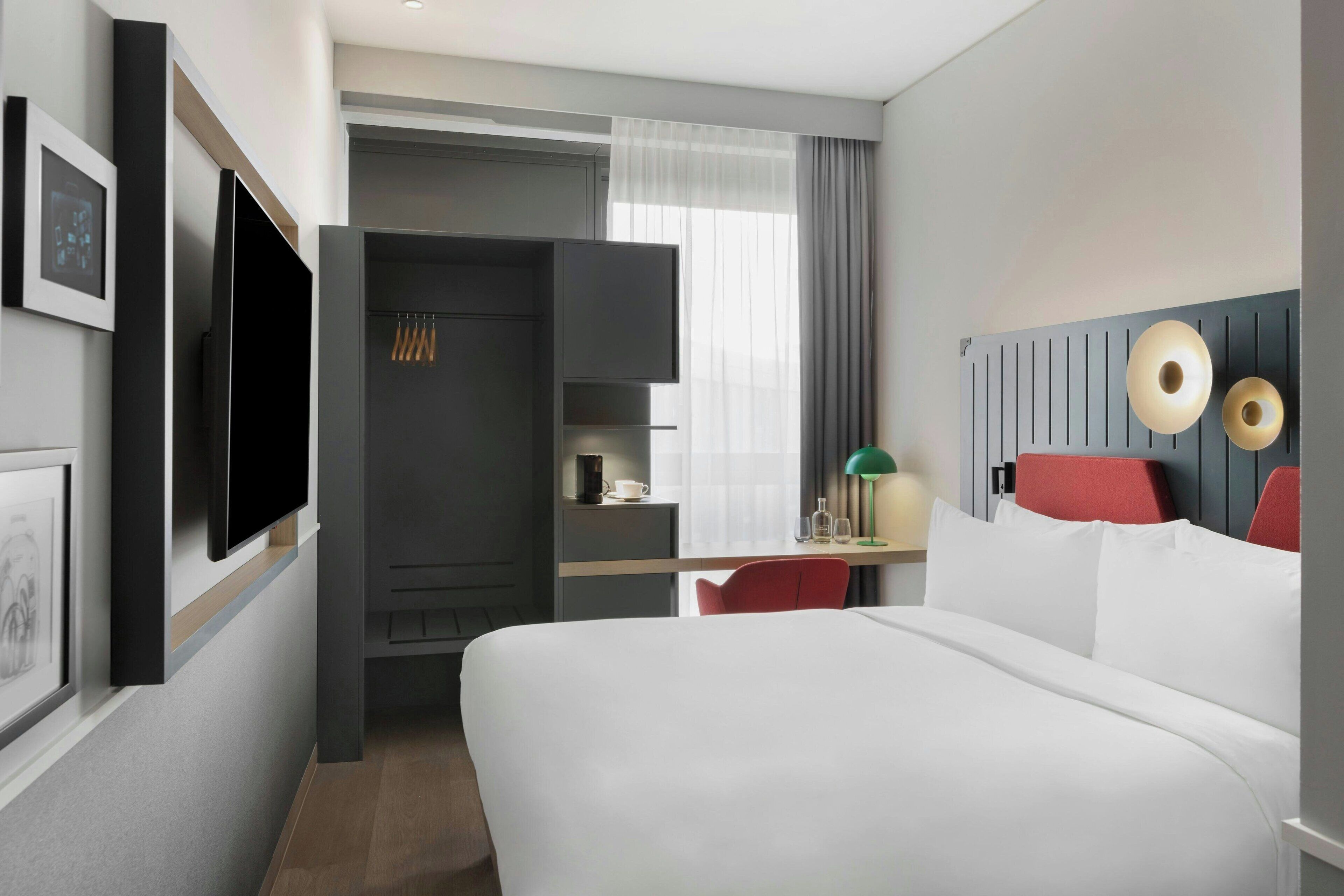Een hotelkamer met een bed, een bureau met stoel, een televisie, een kledingkast en een raam met gordijnen.