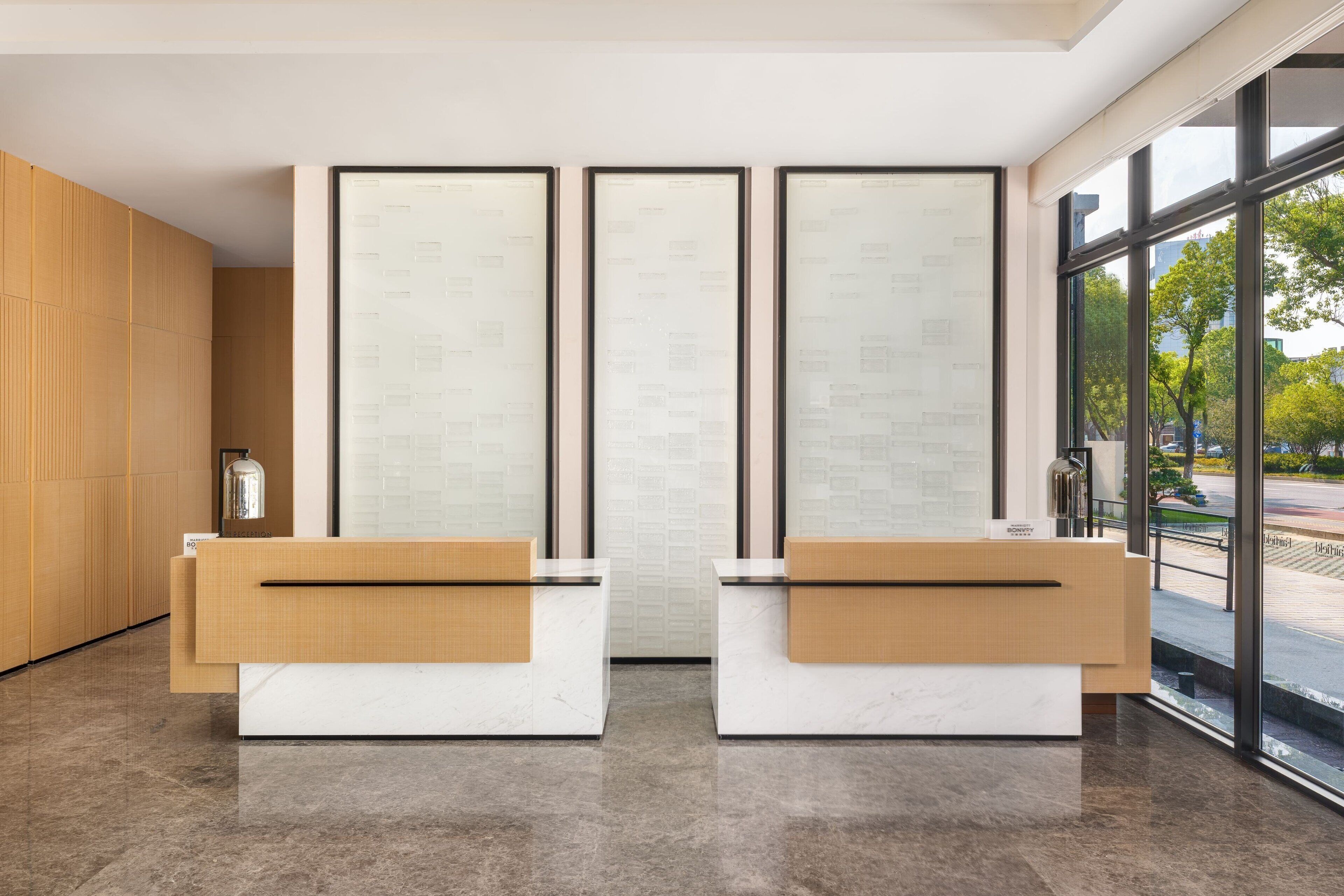 A reception area with two reception desks, a large window with a view of the outdoors, and a wall with framed documents.
