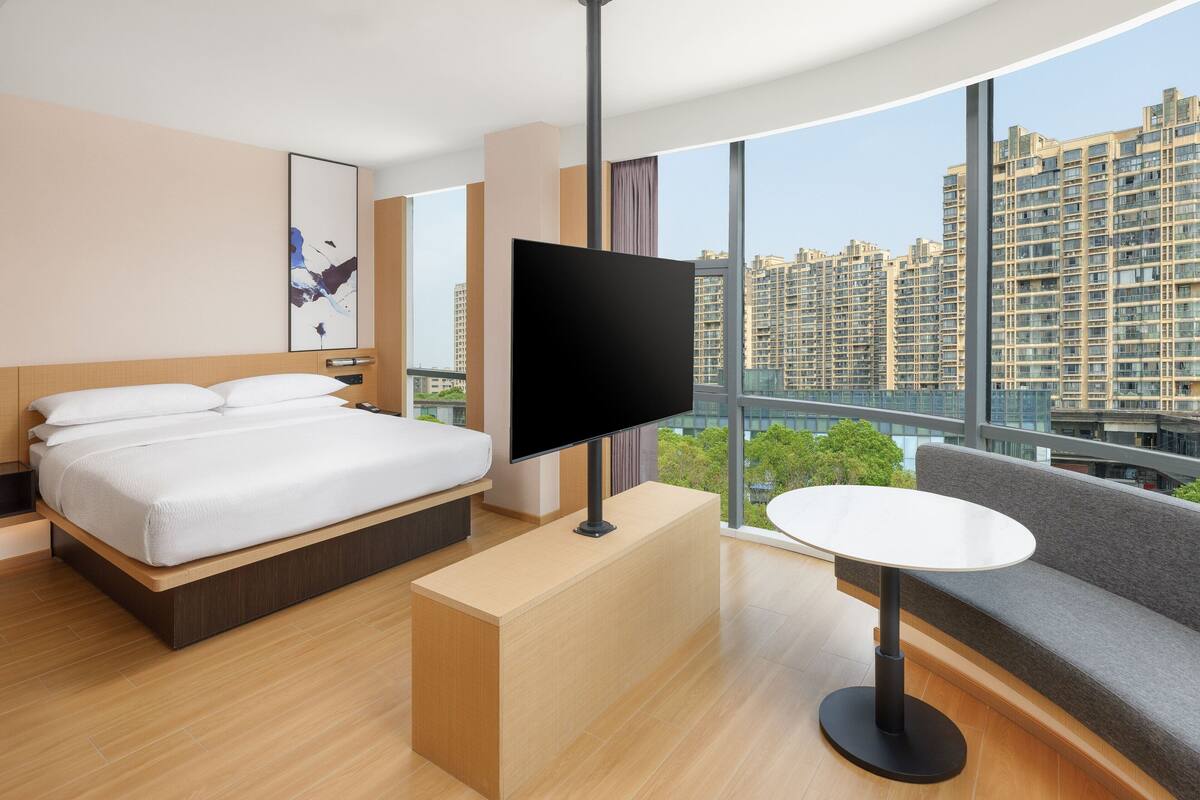 A modern hotel room with a large bed, a flat-screen TV, a small table, and a sofa.