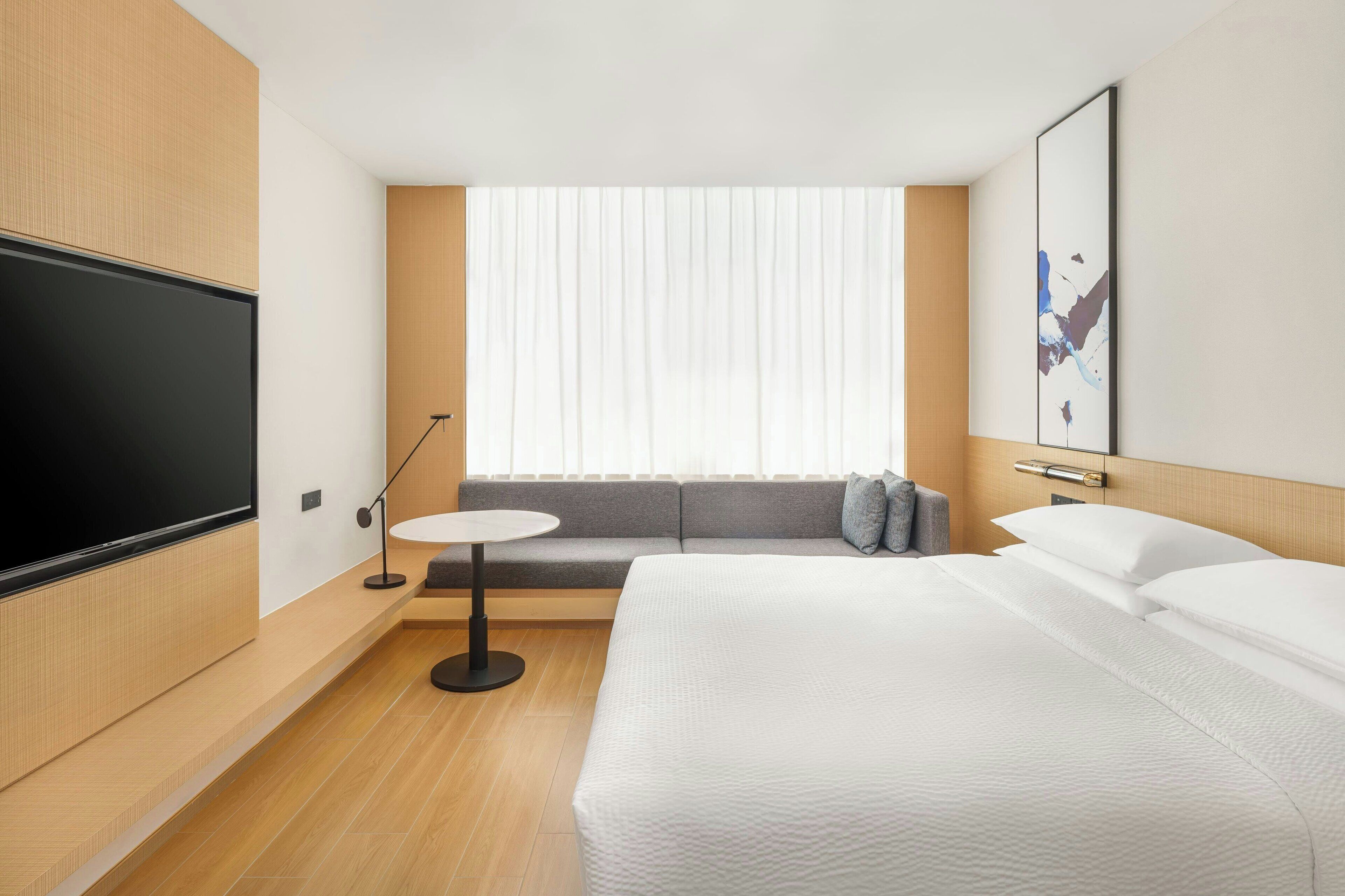A modern hotel room with a large bed, a sofa, a small round table, and a TV mounted on the wall.