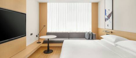 A modern hotel room with a large bed, a sofa, a small round table, and a TV mounted on the wall.
