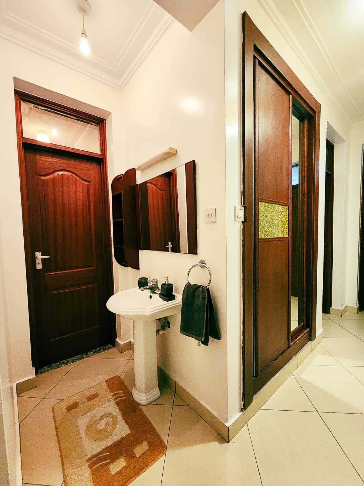 A hallway with a wooden door, a white sink, and a mirror.