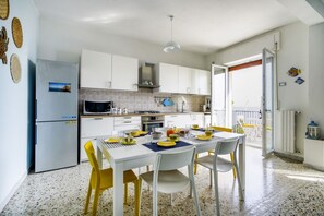 A modern kitchen with white cabinets, a dining table set with yellow chairs, and a view through an open door to an outdoor area.