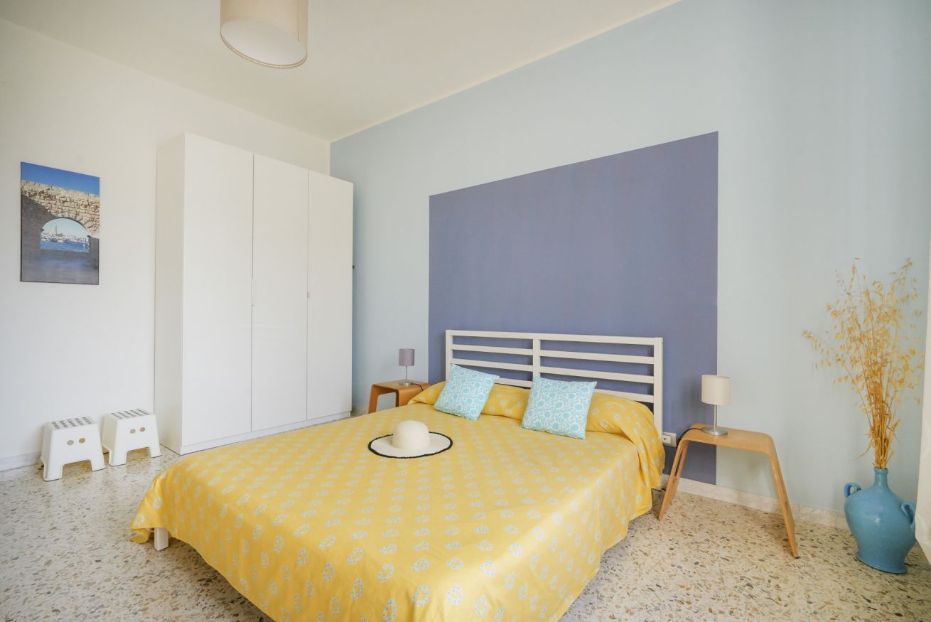 Une chambre à coucher avec un lit, une armoire blanche, une table de chevet, une lampe et un vase contenant des plantes séchées.