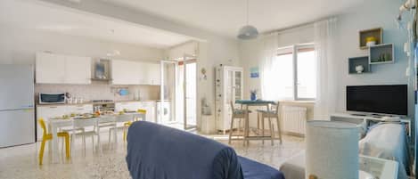 Amplia sala de estar con sofá cubierto, una mesa de comedor con sillas, zona de cocina y televisor.