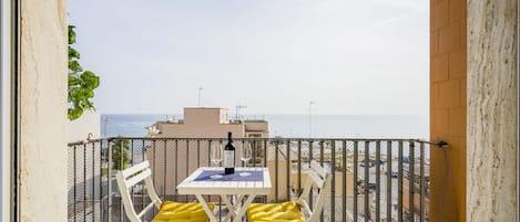 A balcony with a table and chairs, a bottle of wine, and a view of the sea.