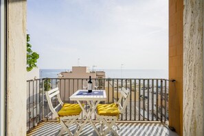 A balcony with a table and chairs, a bottle of wine, and a view of the sea.