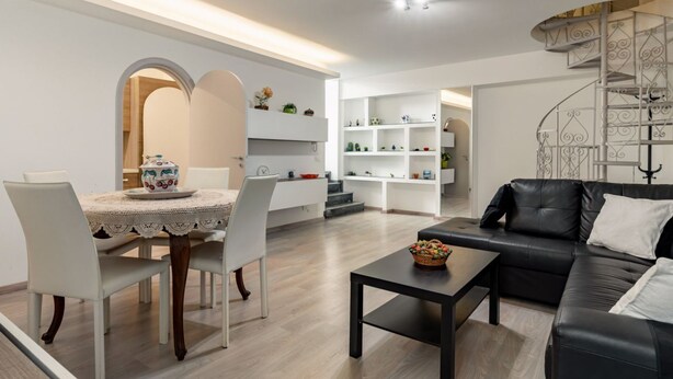 Ein modernes Wohnzimmer mit Essbereich, einem schwarzen Ledersofa, einem Couchtisch und einer Treppe mit einer dekorativen Geländer.