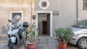 Ein Gebäudeeingang mit einem Schild, auf dem 'Domus Elisio Apartment Taormina' steht, ein abgestellter Roller und zwei Blumentöpfe.