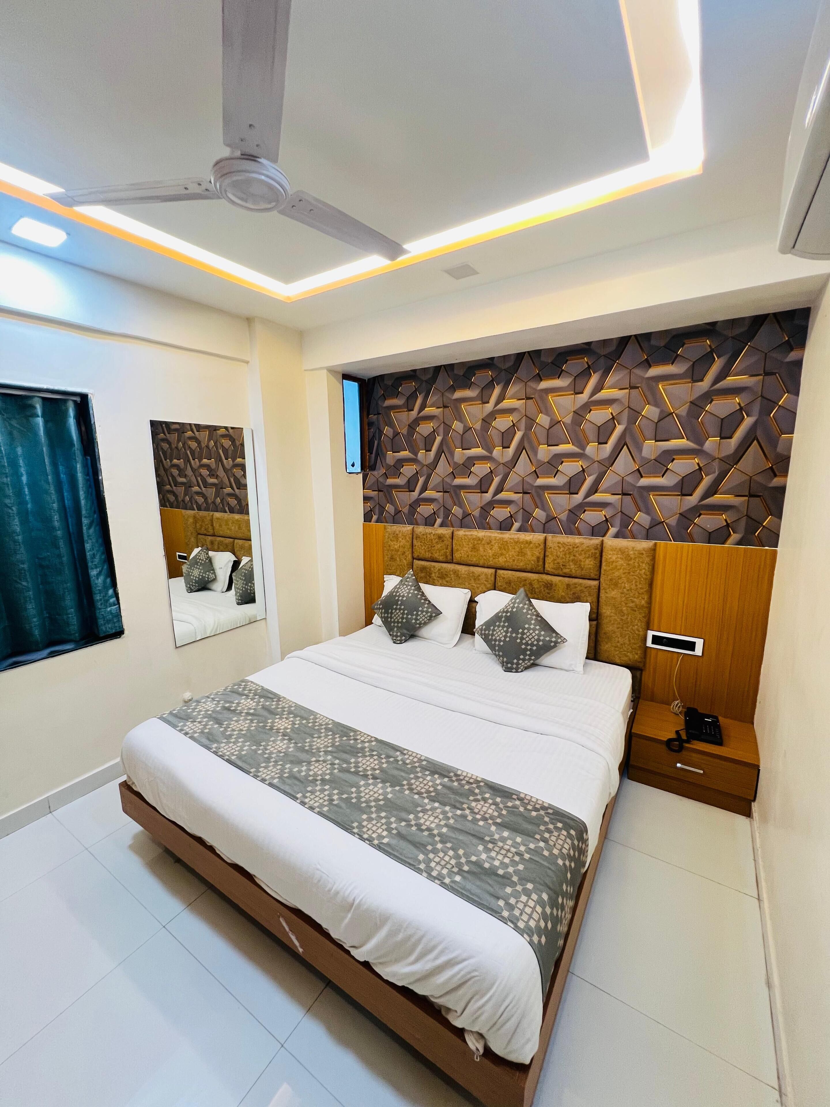 A modern bedroom with a large bed, a ceiling fan, a decorative wall panel, a bedside table with a phone, and a window with curtains.