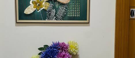 Eine Vase mit bunten Blumen auf einem Fliesenboden, eine Tür und ein gerahmtes Bild an der Wand.