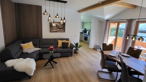 Un salon moderne avec un canapé d’angle, une table à manger avec des chaises et une cuisine en arrière-plan.