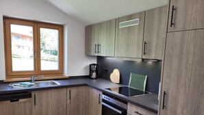 Une cuisine moderne avec des meubles en bois, un four encastré, une machine à café et une fenêtre donnant sur une maison.