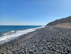 Una spiaggia rocciosa con onde, cielo sereno e una scogliera.
