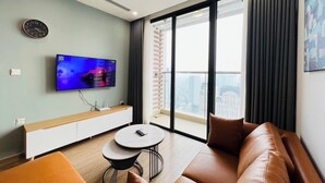 Una sala de estar moderna con un televisor de pantalla plana, un sofá, una mesa de centro y vistas a un paisaje urbano a través de amplios ventanales.