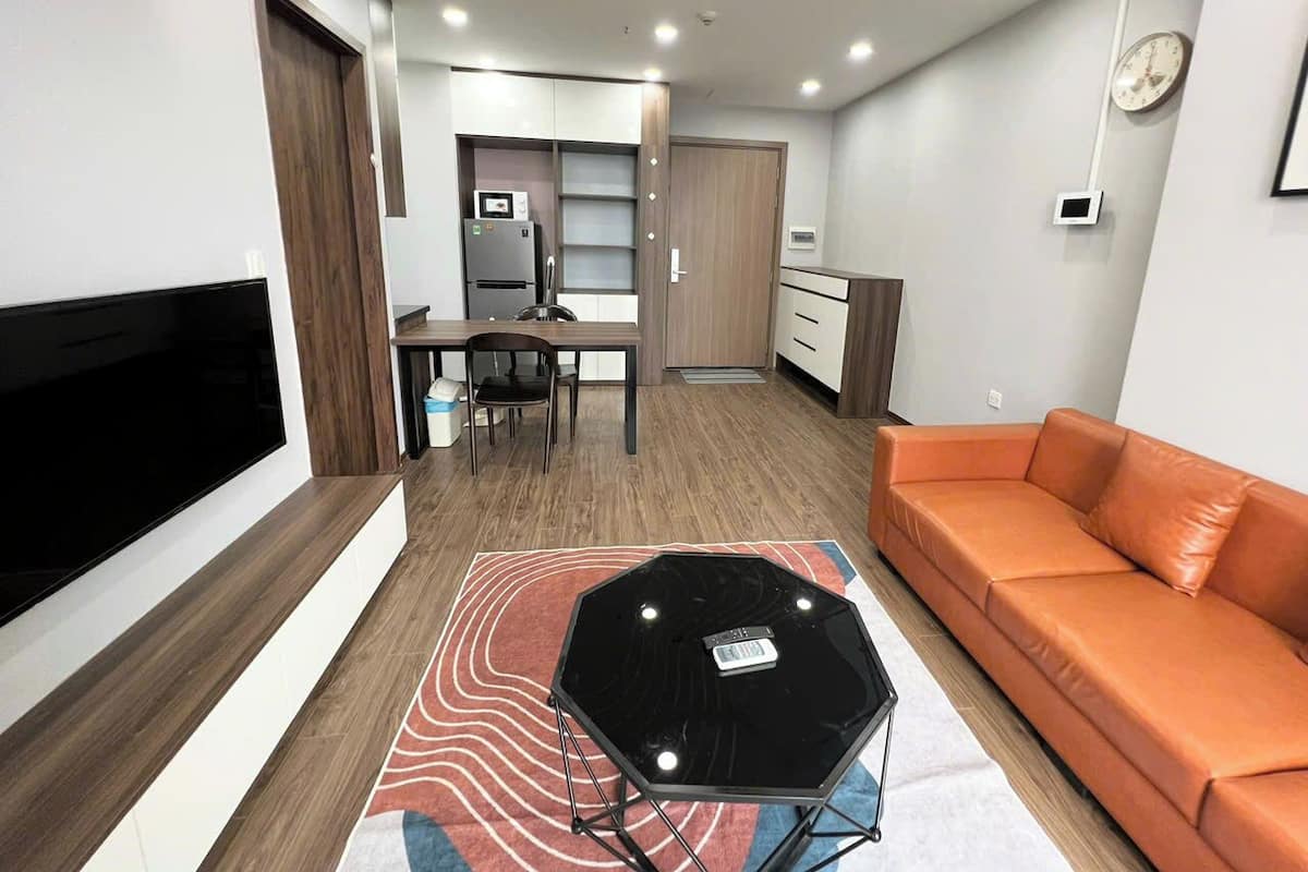Un salon moderne doté d’un téléviseur à écran plat, d’un canapé orange, d’une table basse en verre et d’un coin repas avec une table et des chaises.
