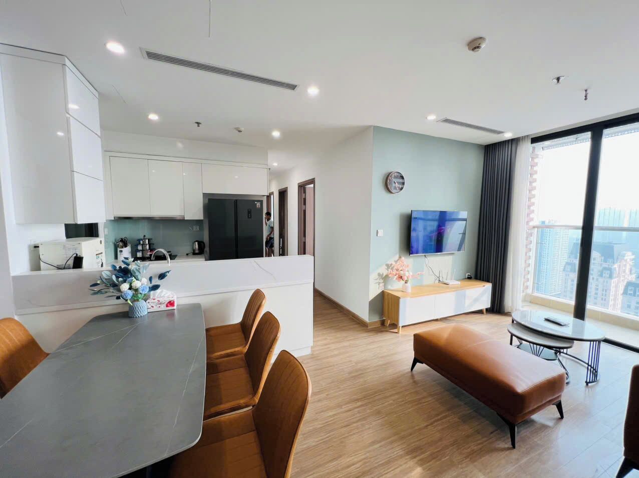 Una sala de estar moderna con comedor, cocina y un amplio ventanal con vista a la ciudad.