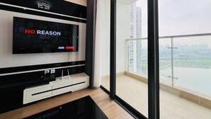 Una sala de estar moderna con un televisor de pantalla plana grande montado en la pared, un mueble blanco de entretenimiento debajo y una vista de la ciudad a través de un ventanal amplio.