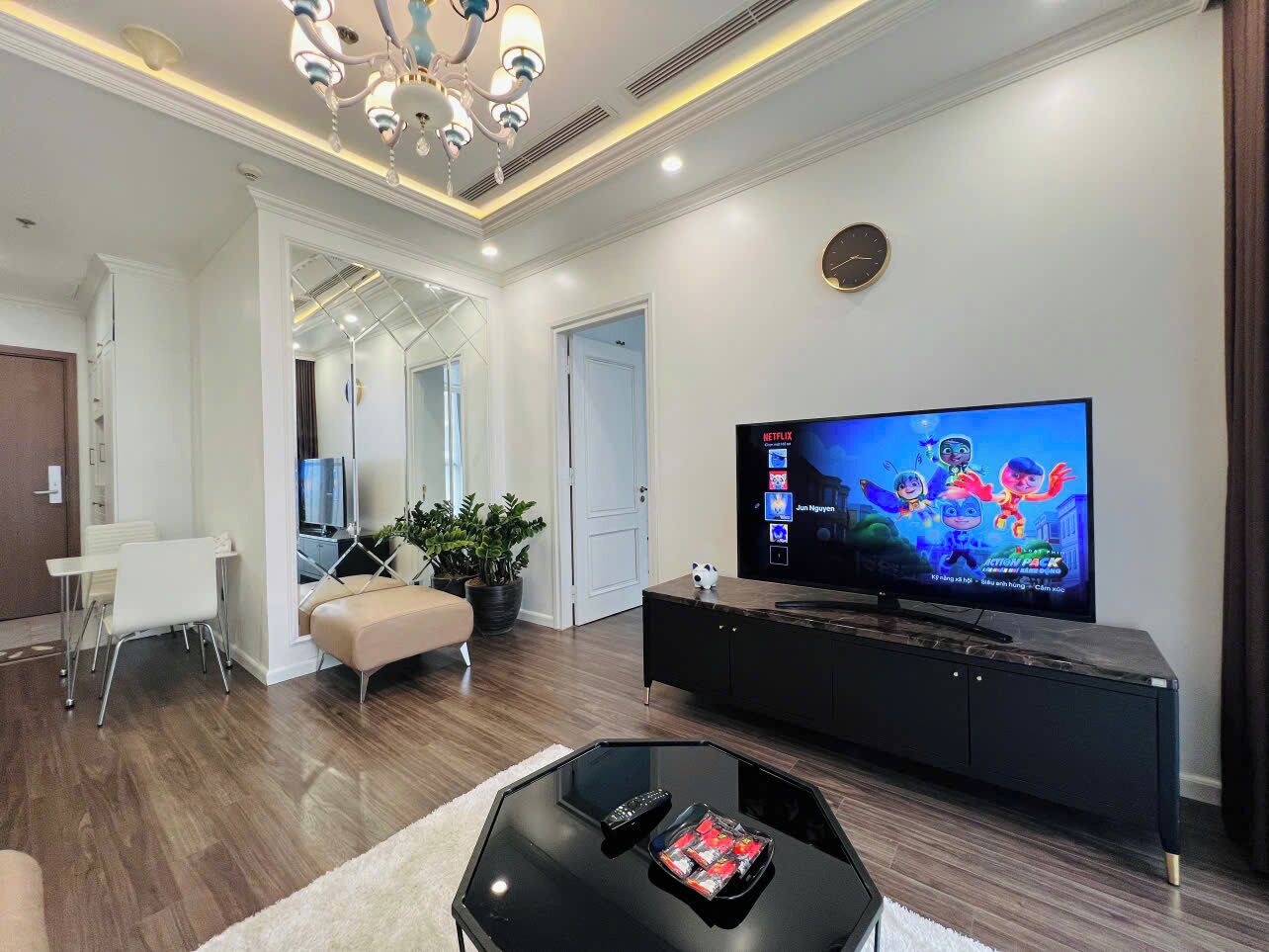 Un salon moderne doté d’un téléviseur à écran plat, d’un meuble de rangement noir, d’une table basse en verre et d’un canapé beige.