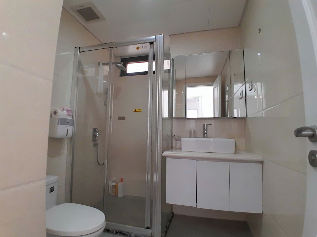A bathroom with a glass-enclosed shower, a toilet, and a sink with a mirror above it.