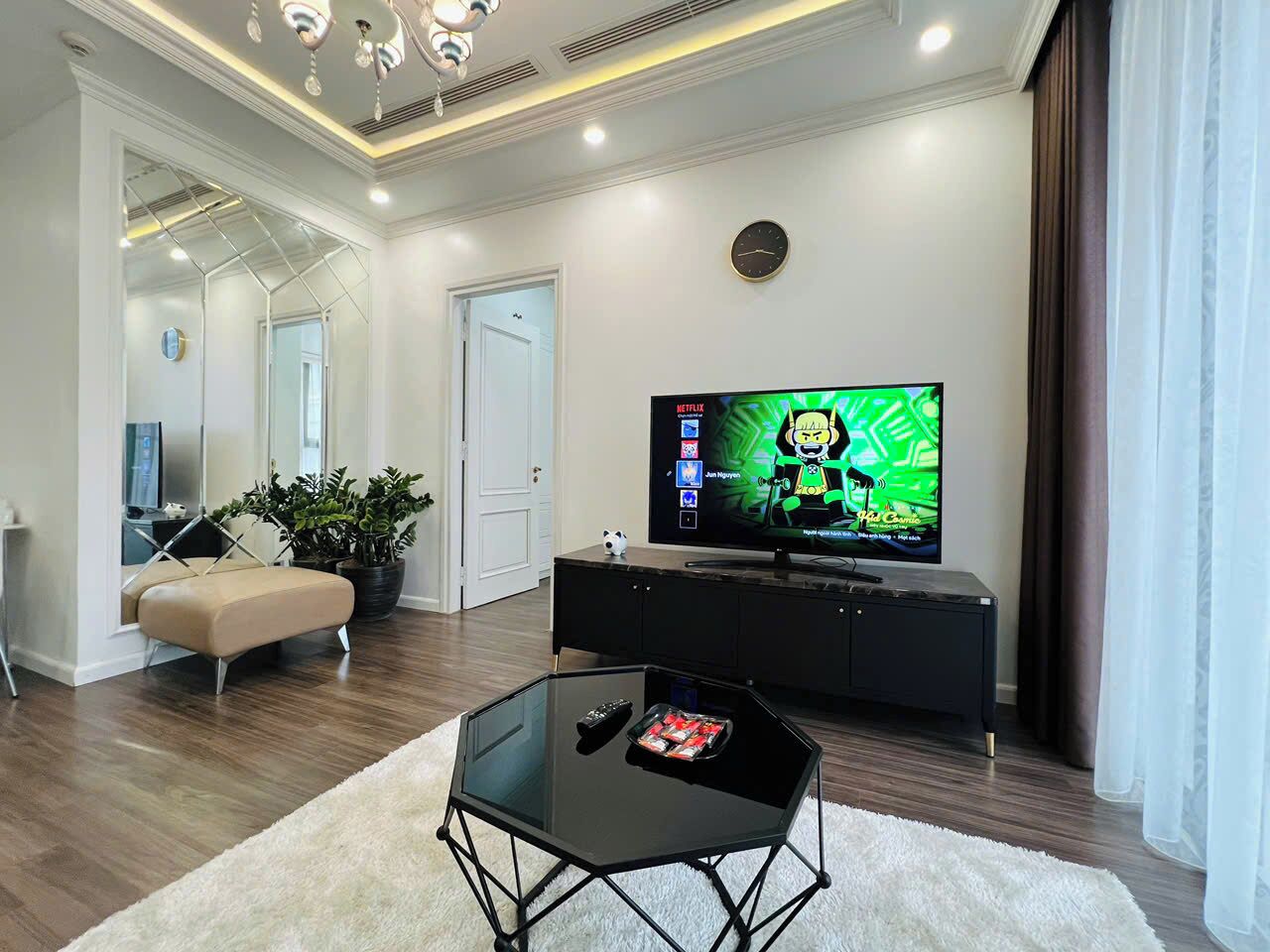 Una sala de estar moderna con una mesa de centro de vidrio, un sofá color beige, un mueble de entretenimiento negro y un televisor de pantalla plana mostrando una caricatura.