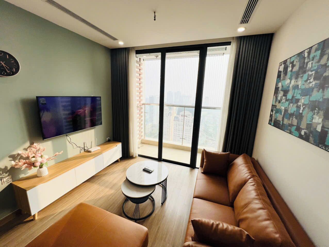 Ein modernes Wohnzimmer mit einer Couch, einem Couchtisch, einem Fernseher und einem großen Fenster mit Blick auf die Stadt.