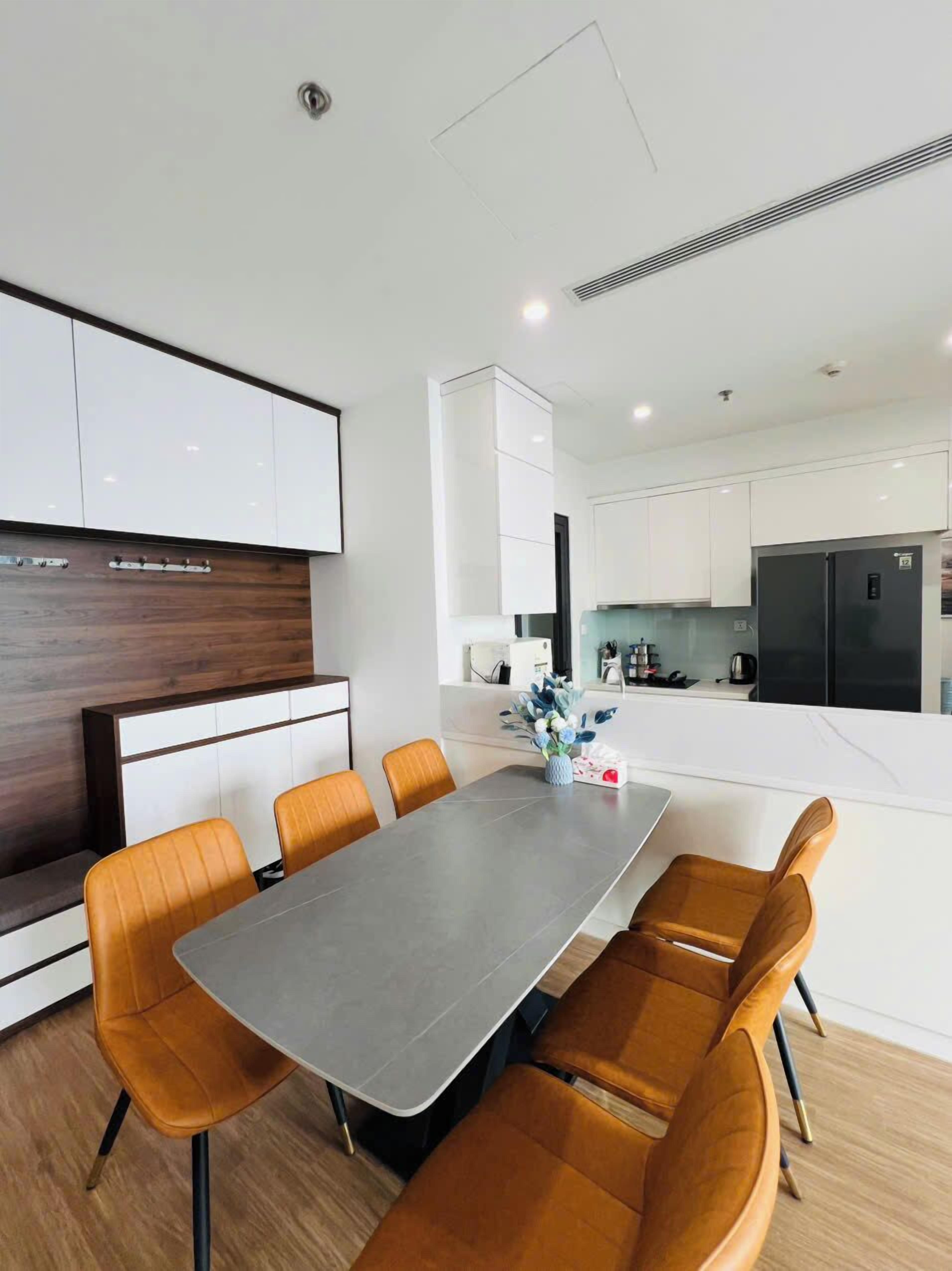 A modern kitchen with white cabinets, a black refrigerator, and a dining area with a grey table and orange chairs.