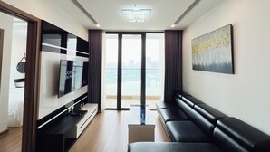 Una sala de estar moderna con un televisor de pantalla plana grande, un sofá de cuero negro y una vista de la ciudad a través de la puerta de vidrio.