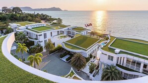 Un complexe hôtelier moderne composé de plusieurs bâtiments dotés de toits végétalisés, d’un jardin aménagé et offrant une vue sur la mer au coucher du soleil.