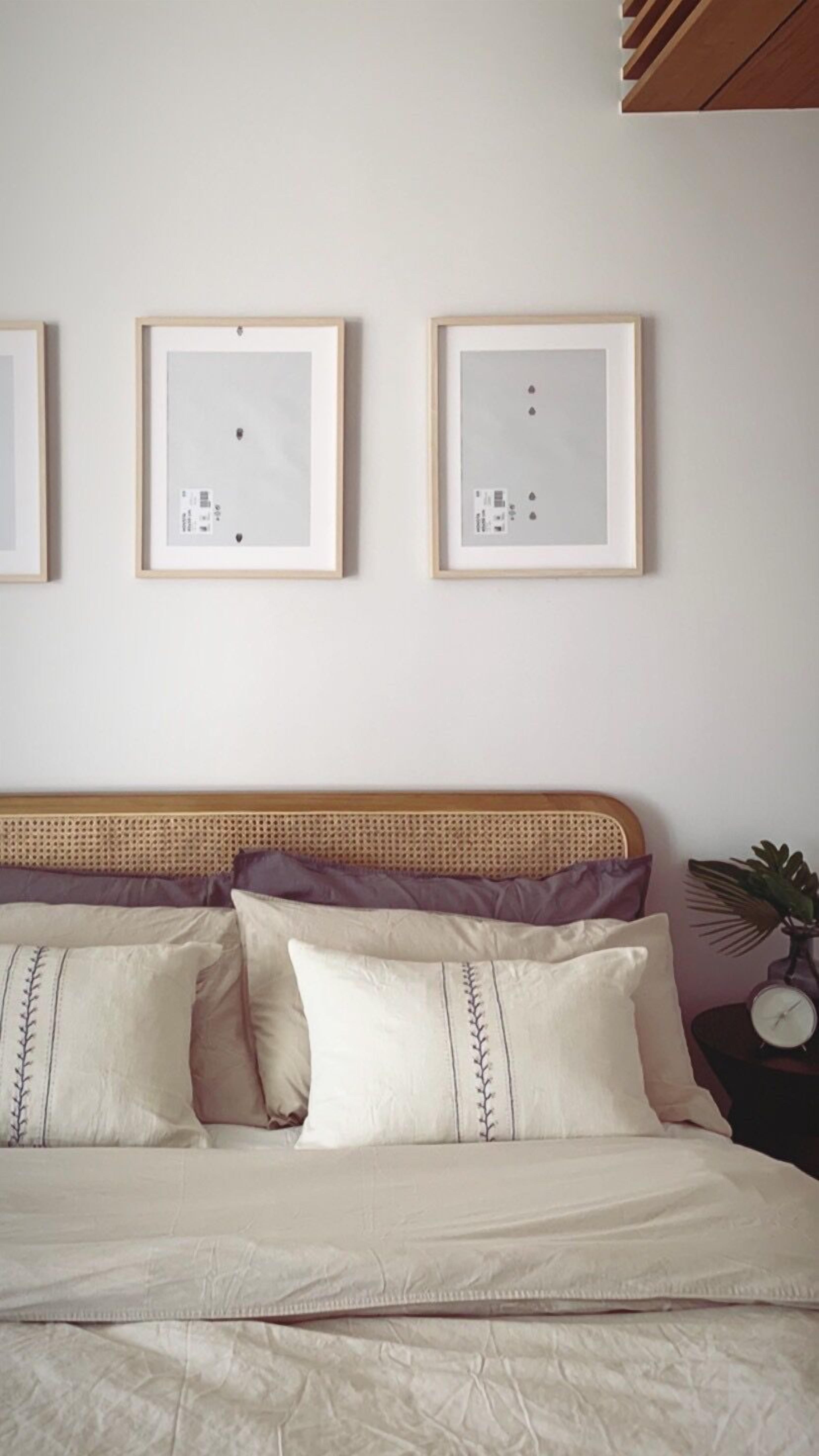 Quarto com cama, almofadas, cabeceira e três quadros na parede.