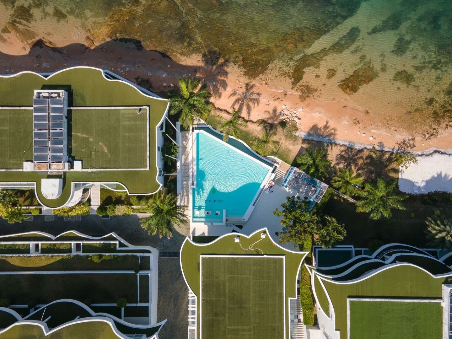 Vue aérienne d’un complexe hôtelier doté d’une piscine, d’un court de tennis et d’une plage.
