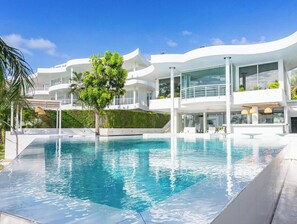 A modern, multi-story building with a large, clear swimming pool in the foreground. - Ocean Beachfront Smart Unit (Sattahip)