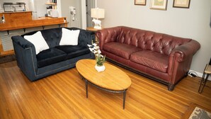 Una sala de estar con un sofá azul oscuro, un sofá de cuero rojo y una mesa de centro de madera.