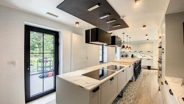 Una cocina moderna con una isla grande, iluminación colgante y vistas a través de un ventanal.