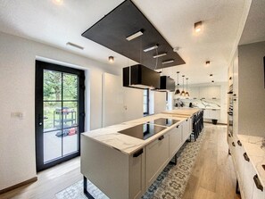 A modern kitchen with a large island, pendant lighting, and a view through a glass door.