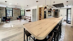 Una cocina amplia con una isla de madera alargada, iluminación colgante y una pared de acento de piedra.