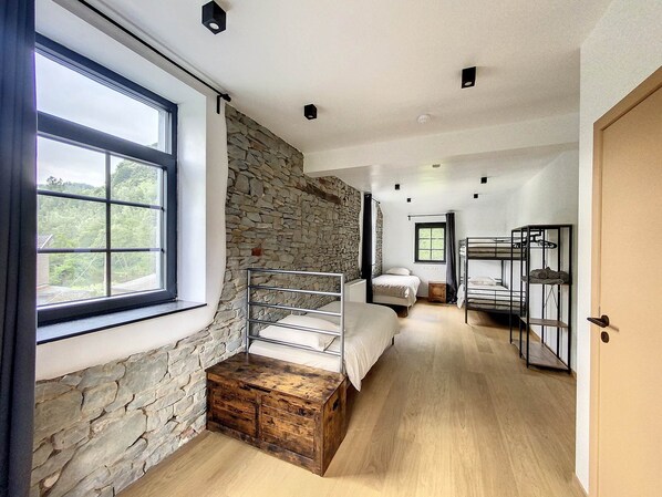 A narrow hallway with bunk beds, a stone wall, and a large window.