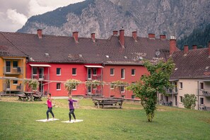 A courtyard with two people practicing yoga, surrounded by buildings with red and yellow facades, and a mountainous backdrop. - Styria Apartment near hiking trails (No Deposit) (Eisenerz)