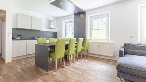 A modern kitchen with white cabinets, a dining table with green chairs, and a grey sofa in a bright room with wooden flooring. - Nice apartment in Stryia with sauna (No Deposit) (Eisenerz)