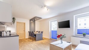 Eine moderne Küche mit Essbereich, einem an der Wand montierten Fernseher und einem Fenster mit Jalousien.