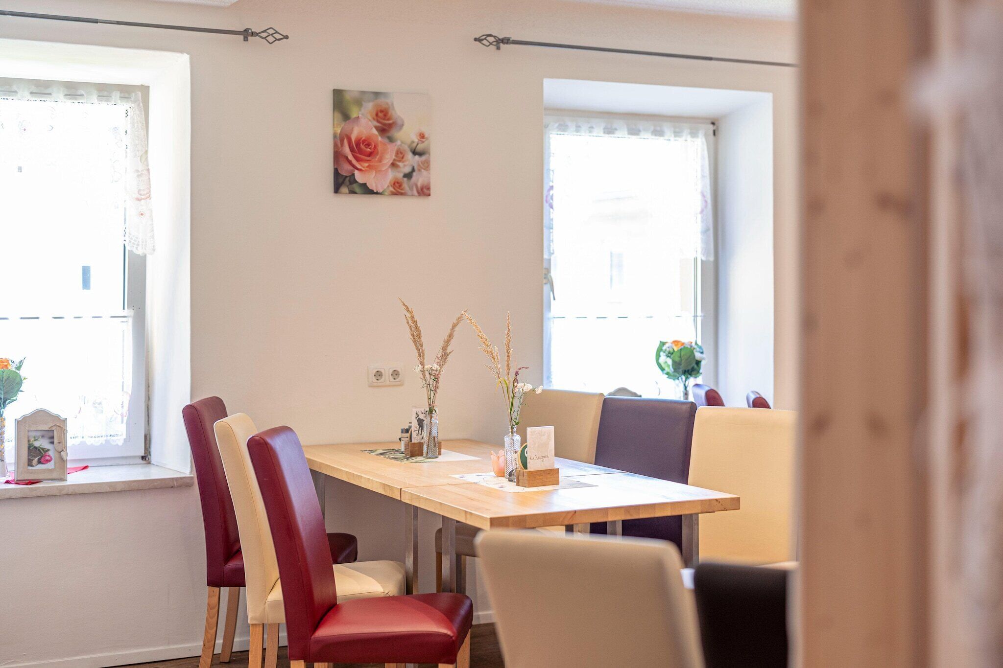 A dining area with a wooden table, red and beige chairs, and two vases with dried plants.