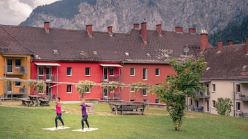Une cour bordée d’un bâtiment rouge, d’un bâtiment jaune et dominée par une chaîne de montagnes en arrière-plan.