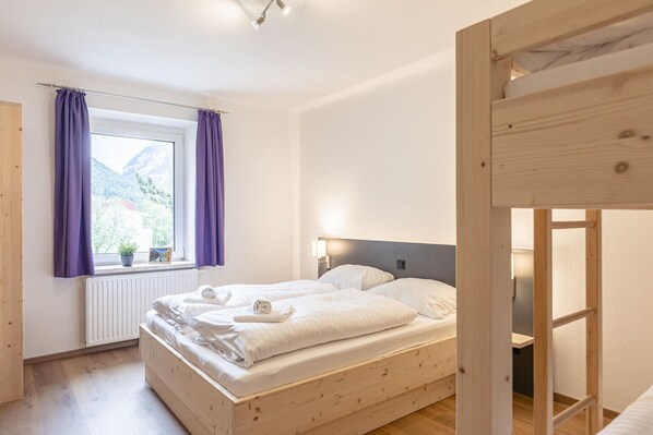 Une chambre avec un lit en bois, une fenêtre avec des rideaux, un radiateur et une vue sur les montagnes.
