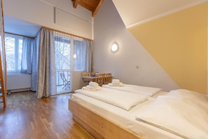A bedroom with a wooden bed, a small table with chairs, and a balcony with a view.