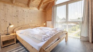 Een houten slaapkamer met een bed, nachtkastje en een raam met gordijnen.