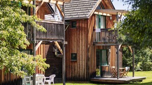 Een houten chalet met een balkon, een klein terras en een trap naar een bovenverdieping.