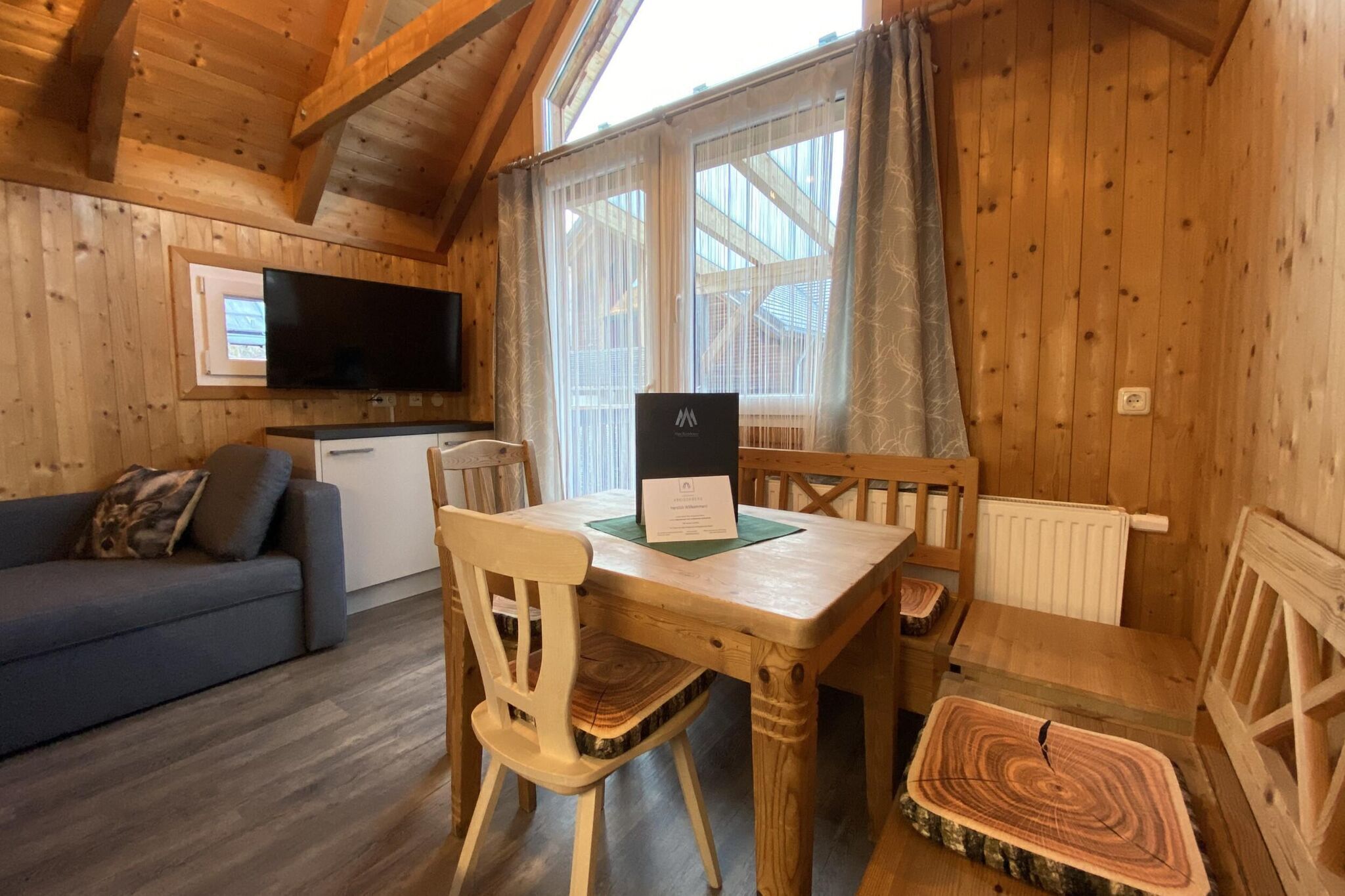 Ein gemütliches Holzhaus mit Essbereich, einer Couch und einem an der Wand befestigten Fernseher.