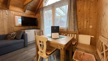 Ein gemütliches Holzhaus mit Essbereich, einer Couch und einem an der Wand befestigten Fernseher.