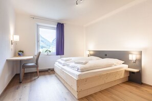 Une chambre avec un lit en bois, un bureau et une fenêtre donnant sur les montagnes.