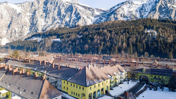 A town with traditional architecture, a central yellow building, and a mountain backdrop.